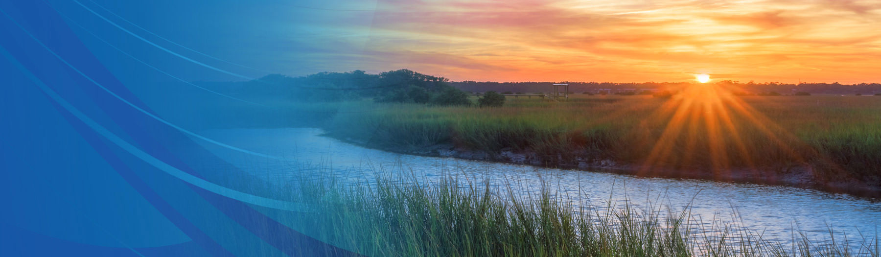 Sun setting over a beautiful landscape with a river and tall grass in the foreground