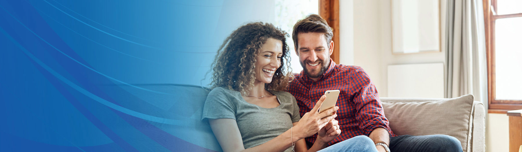 A woman and a man sitting together on a couch, looking at a mobile phone screen