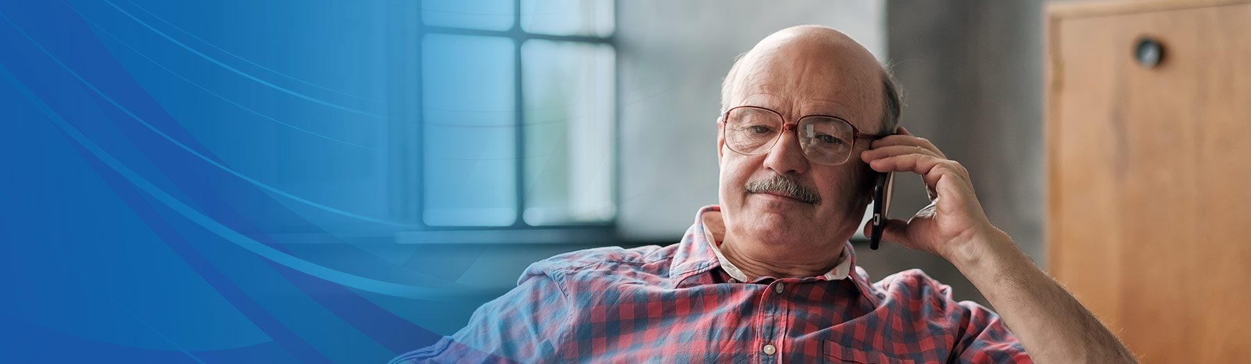 Older gentleman wearing a plaid shirt is talking on his cell phone at home