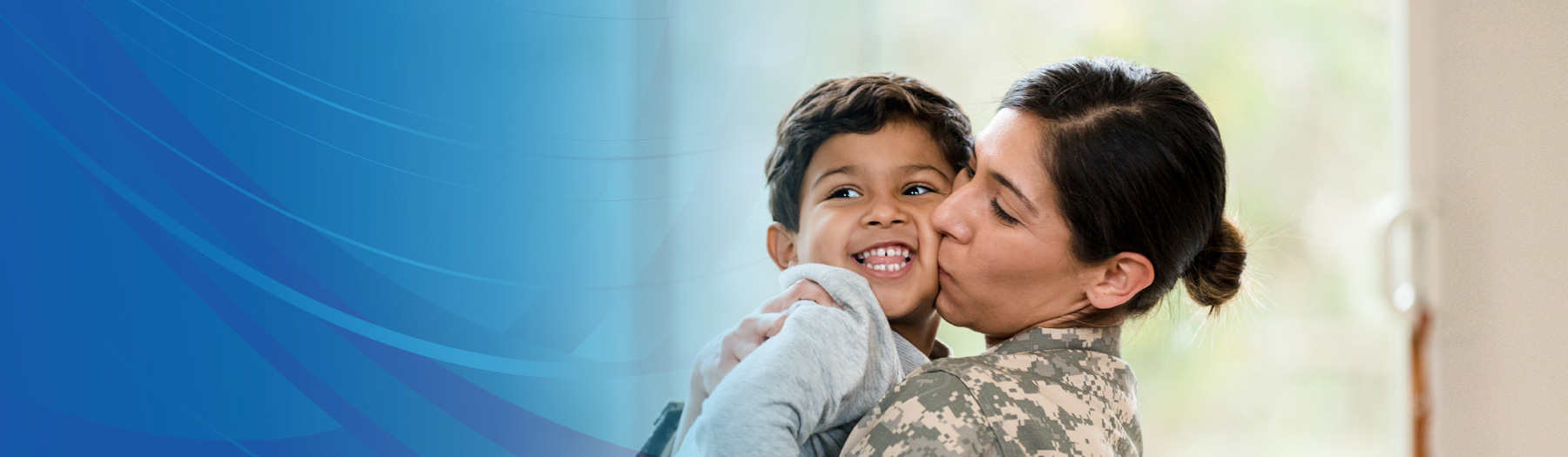 Mother wearing military camouflage hugs and kisses smiling young son