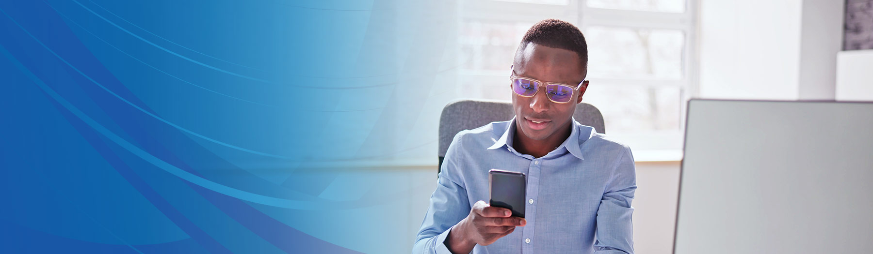 Professional businessman looks at his mobile phone while sitting at a desk with a computer