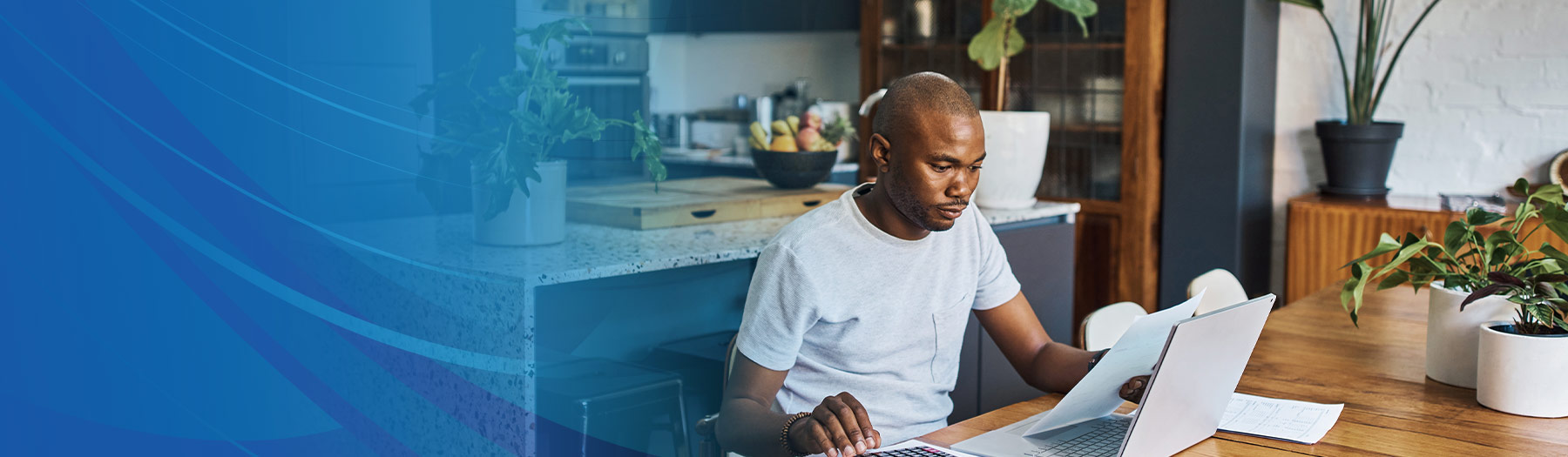 Man at home, sitting at table, reviewing financial documents at his computer